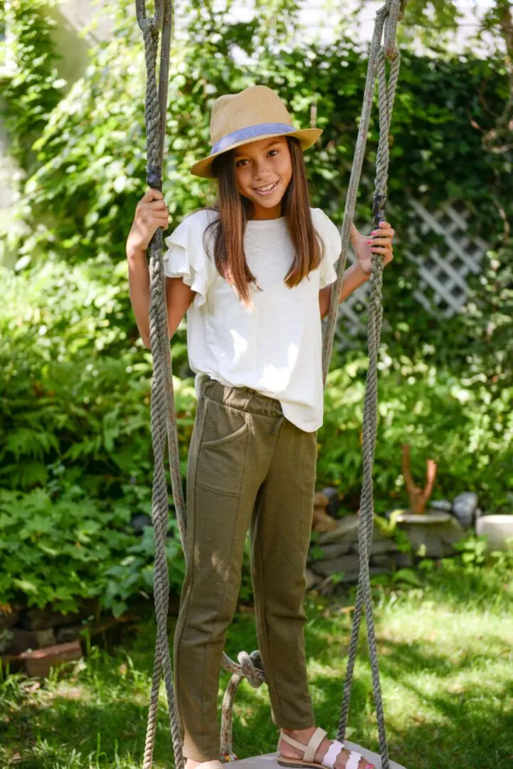 A teen wearing a white top, brown jogger pants, and a brown bucket hat standing on a giant swing