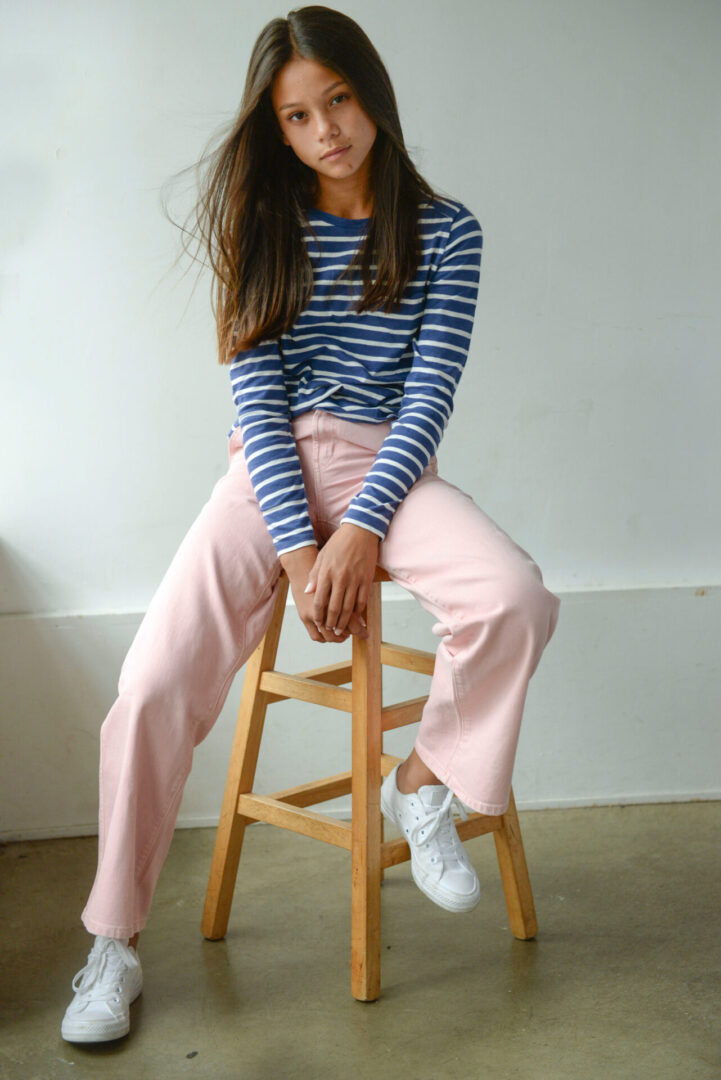 Caroline Quinn wearing stripped shirt and sitting on stool